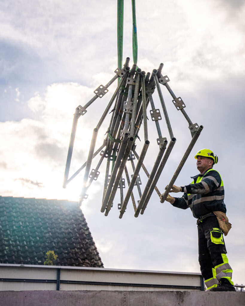 Mit dem Kran werden Gerüstbauteile auf die Baustelle geliefert