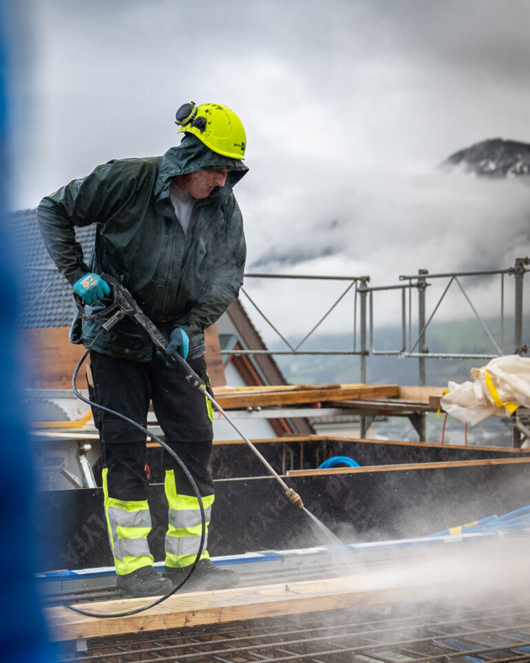 Arbeiter in Regenkleidung arbeitet mit einem Hochdruckreiniger