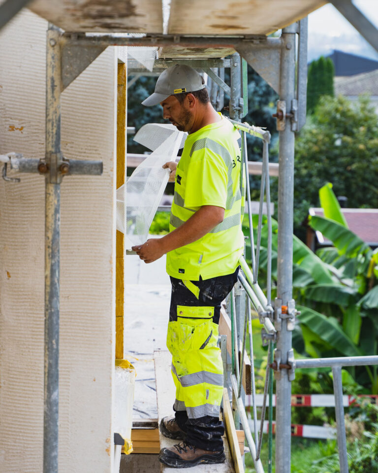 Ein Gipser steht auf einem Gerüst und begutachtet die frisch verputzte Aussenfassade.